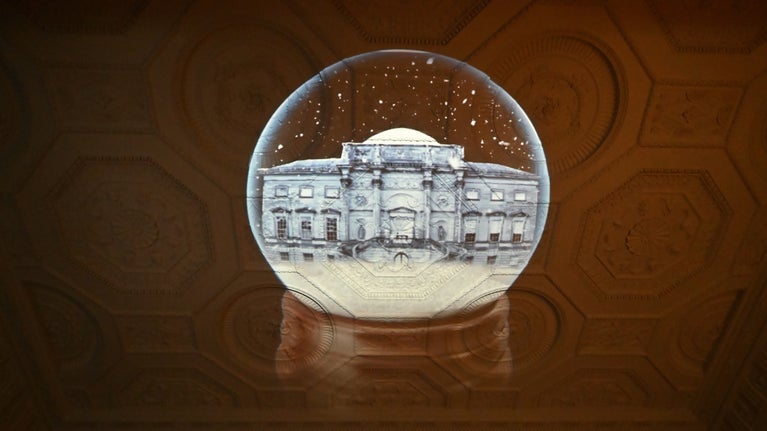 A light projection of a grand house shines on an ornate ceiling